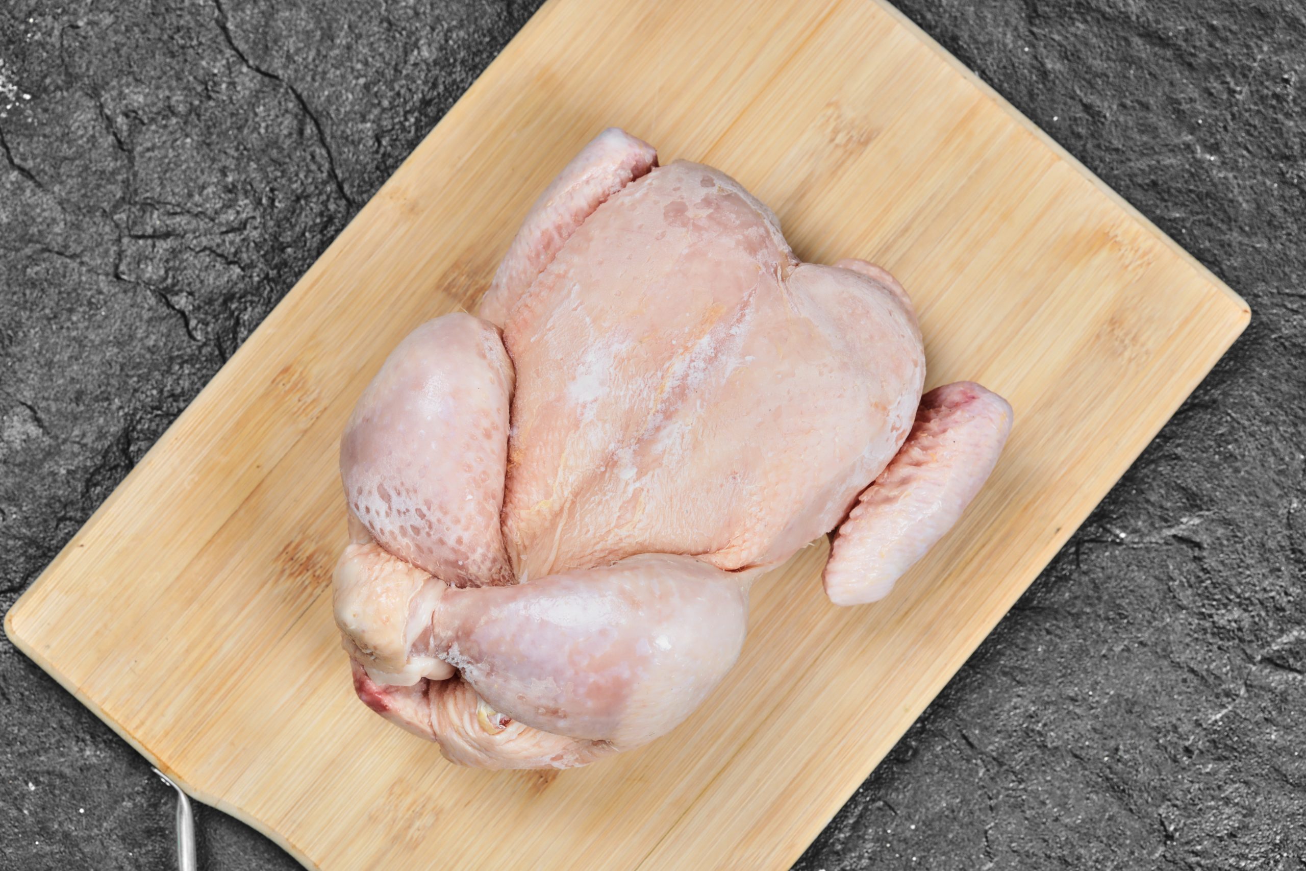 pollo entero crudo sobre una tabla de cortar de madera