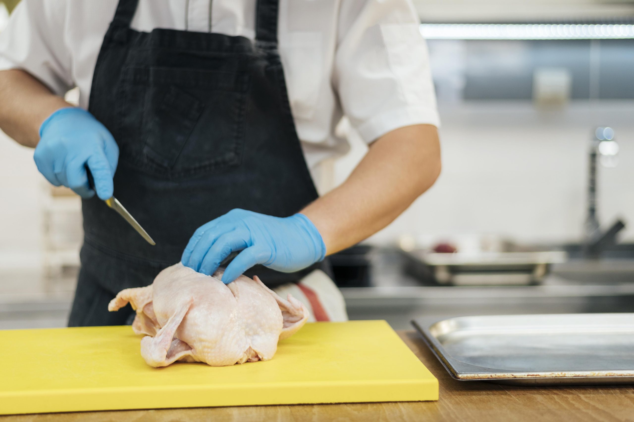 vista frontal del chef con guantes cortando pollo